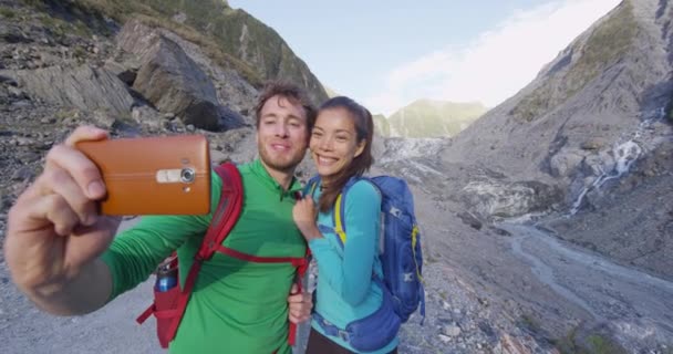 Selfie pareja tomando teléfono autorretrato en Nueva Zelanda por Franz Josef Glaciar — Vídeo de stock