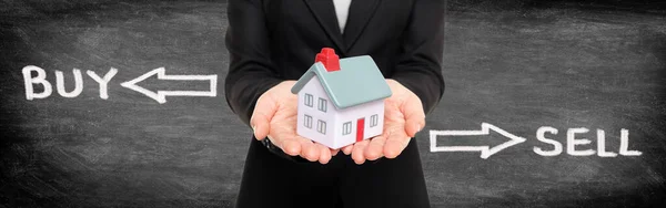 부동산 중개업자는 주택 시장의 개념을 사고 팔기 위해 소형 주택을 전시한다. 검은 칠판 위에 그래픽 디자인으로 집을 잡고 있는 파노라마 현수막. — 스톡 사진