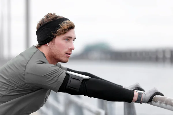 Winter running man runner training outside using phone holder listening to music with headband cold weather accessories wearing wearable tech smartwatch — Stok Foto