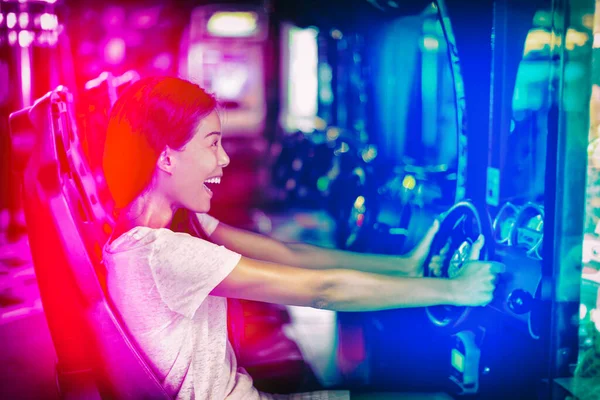 日本のゲームサイバーカフェの女の子ゲーマーは楽しいゲームを持っている。レーシングカーゲームの楽しさを運転するアジアの女性は、ビデオゲームの仮想スポーツカーアーケードマシンをプレイ. — ストック写真