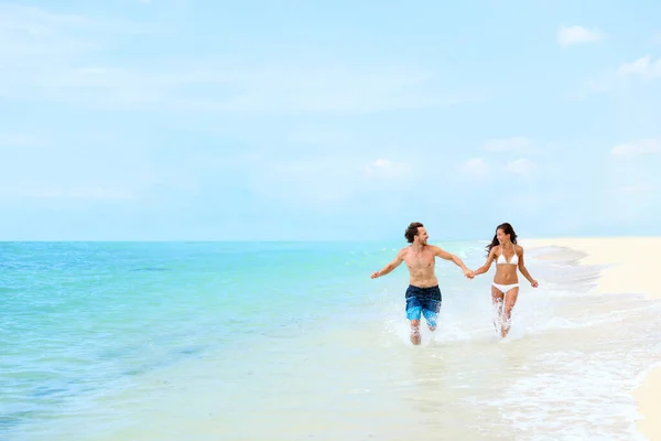 Férias na praia casal feliz correndo água espirrando no oceano azul se divertindo no destino do Caribe viagens de verão. Turistas desfrutando de férias relaxante rindo juntos de mãos dadas. — Fotografia de Stock