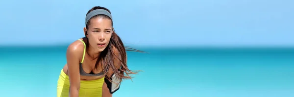 Tired running Asian woman listening to music or podcast with wireless earbuds wearing phone armband holder during beach run sweating on summer workout. Heat stroke breathing fitness girl banner. — Stock Photo, Image