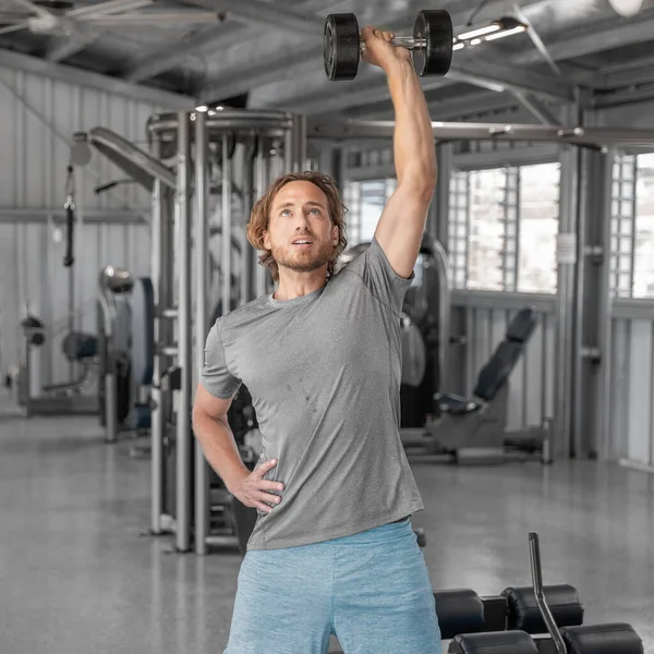 Siłownia fitness trening człowieka z hantlami podnoszenie nad głową podnoszenie ramion ćwiczenia prasa ramienia w pomieszczeniach w siłowni. Kwadrat. — Zdjęcie stockowe