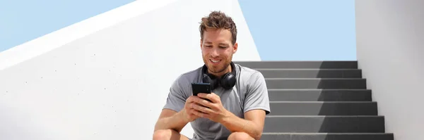 Young fit man met behulp van mobiele telefoon app voor online streaming van muziek luisteren met draadloze hoofdtelefoon banner panoramisch. Stad levensstijl. — Stockfoto