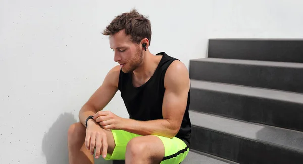 Smartwatch usando o homem que se conecta a fones de ouvido sem fio para ouvir música durante o treino de corrida. Corredor atleta com tecnologia wearable relógio de esportes no ginásio de fitness. — Fotografia de Stock