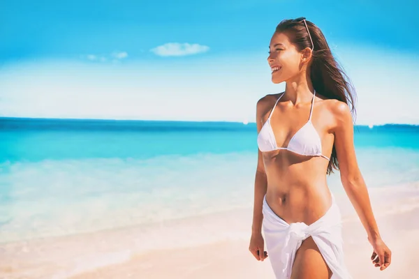 Bikini Mujer asiática en traje de baño blanco caminando en vacaciones en la playa del océano para el lujo spa de bienestar. Tratamiento láser depilación cuerpo listo verano. Chica usando pareo falda ropa de playa. — Foto de Stock