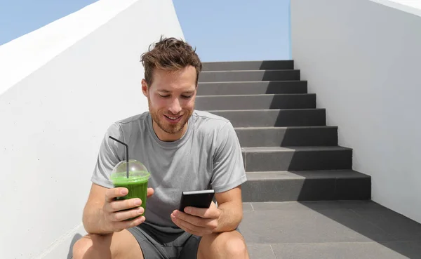 Green smoothie juice drink man drinking detox diet protein shake using mobile phone app for tracking nutrition diet meal plan. Estilo de vida saudável. — Fotografia de Stock