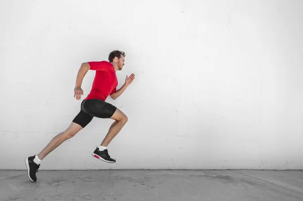 Fitness running hombre corredor perfil en la pared de fondo blanco. Atleta deportivo masculino corriendo con entrenamiento de entrenamiento de intervalos de alta intensidad hiit usando ropa de ropa deportiva de compresión. — Foto de Stock
