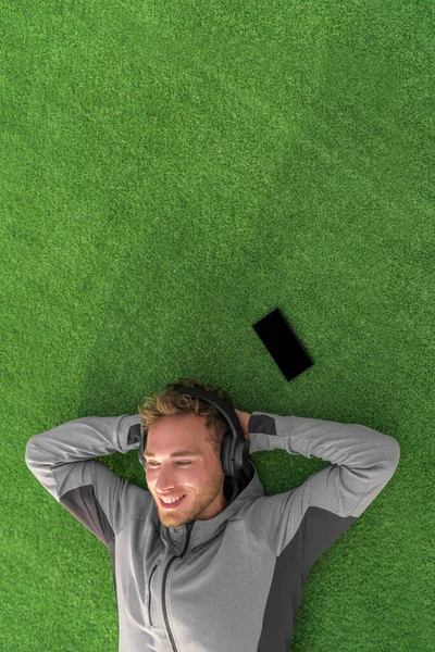 Écouter de la musique pour se détendre. Homme heureux couché sur l'herbe profiter podcast sur téléphone mobile avec casque sans fil. Style de vie estival — Photo