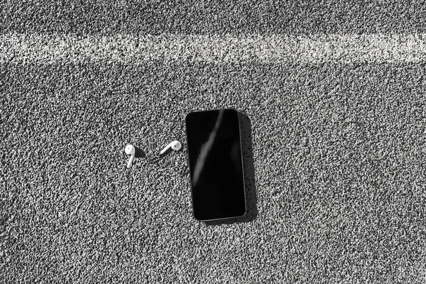 Bezprzewodowa technologia noszenia w słuchawkach dousznych z telefonem komórkowym widok z góry na miejskiej ulicy tekstury tła. Czarny ekran na smartfonie — Zdjęcie stockowe