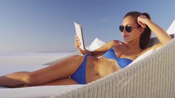 Woman reading book on e-book e-reader tablet relaxing in sofa chair — Stock Video