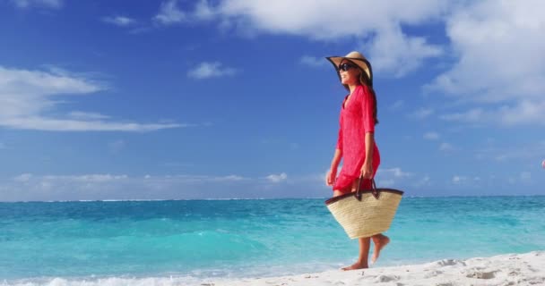 Turystka spacerująca po tropikalnych letnich wakacjach w kapeluszu, czerwonej sukience i torbie plażowej relaksująca się podczas wakacji. Młoda dama w luksusowych strojach plażowych. SŁUGA MOTION VIDEO — Wideo stockowe