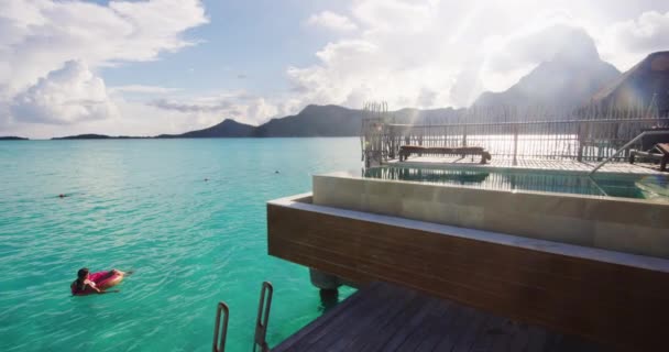 Beach dovolená žena relaxace v bazénu plovák kobliha nafukovací kroužek plovoucí na tyrkysové oceán vody pozadí ve Francouzské Polynésii cestování letní luxusní resort na Bora Bora — Stock video