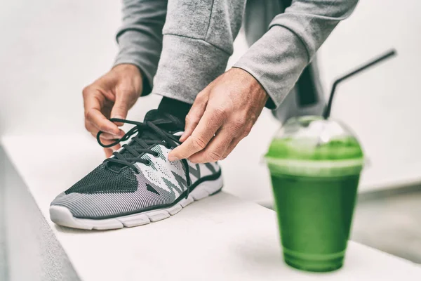 Yeşil meyve suyu sporcusu antrenmana hazırlanıyor koşu ayakkabısı bağcıkları bağlıyor meyve suyu içiyor. Spor ayakkabısı bağlayan spor koşucusu, sebze detoksuyla meyve suyunu temizler sağlıklı beslenir. — Stok fotoğraf