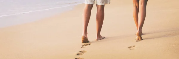 Strand paar lopen op blote voeten op zand bij zonsondergang wandeling huwelijksreis spandoek - vrouw en man ontspannen samen voetafdrukken in het zand. — Stockfoto