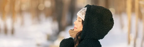Winter vrolijke vrouw ontspannen ademen koude lucht buiten jongeren levensstijl. Aziatisch meisje met gesloten ogen ademhaling wellness en gezondheid in bos dragen capuchon jas en hoed panoramische banner — Stockfoto