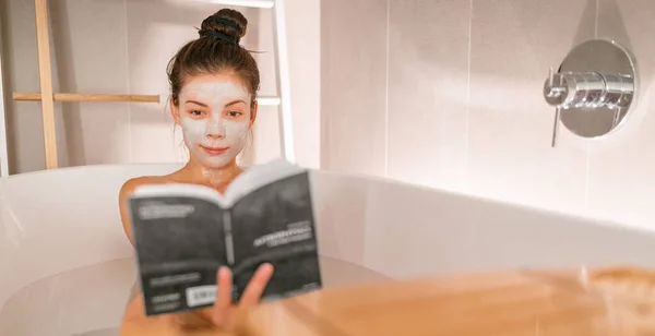 Woman reading book in warm bathtub taking a bath relaxing at home - pamper wellness Asian girl pampering skin care with facial mask treatment banner panorama — ストック写真