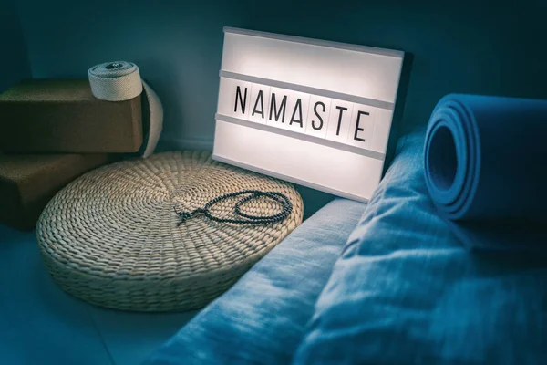 Aula de estúdio de ioga sinal lightbox com letras escrevendo NAMASTE brilhando na luz da noite com acessórios naturais, tapete de borracha, blocos de cortiça, alça de algodão orgânico e travesseiros, travesseiro de meditação de palha — Fotografia de Stock