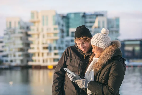 Kış yürüyüşünde cep telefonu kullanan bir çift sokakta yürürken online uygulamadan talimatlara bakıyor. Mutlu Asyalı kadın ve beyaz adam — Stok fotoğraf