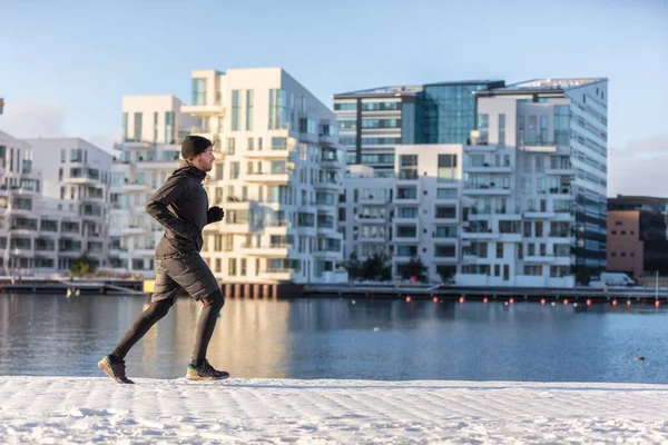 Winter run city lifestyle runner athlete man jogging outside on modern urban harbour street waterfront. Running active living healthy people