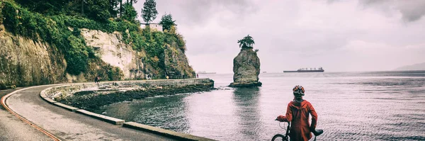 Stanley Park 'ta bisiklet yolunda Vancouver bisikletli bir kadın. İngiliz Kolombiya, Kanada' da ünlü siwash rock, turistik etkinlik. Panorama panoraması. Şehirde bisikletçi var.. — Stok fotoğraf