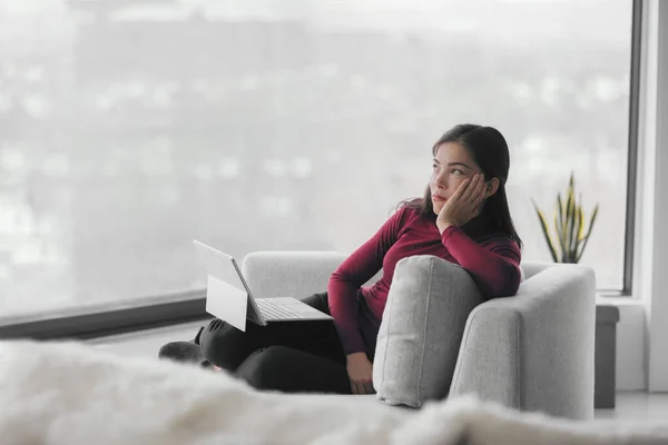 Evde çalışmak dizüstü bilgisayarla tek başına sıkılmış. Erteleme, yorgun Asyalı genç kadın oturma odasındaki bilgisayarda uzaktan kumandayla çalışıyor. Koronavirüsten dolayı hapis. — Stok fotoğraf