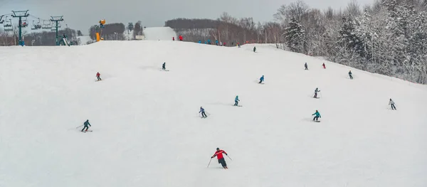 Вид на горнолыжный склон с лыжниками и сноубордистами, быстро спускающимися вниз. Горнолыжный спорт и сноуборд. Панорамный вид на зимние виды спорта — стоковое фото