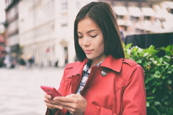 Telefon asiatische Geschäftsfrau SMS auf Handy-App in der Stadt Straße, urbanen Lebensstil. Europas Reisetouristen reisen mit dem Smartphone draußen herum. Chinesische Geschäftsfrau im roten Trenchcoat — Stockfoto