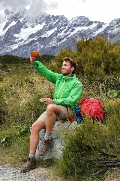 纽西兰猕猴在库克山的胡克山谷小径上徒步旅行时拍下了自拍的手机照片。徒步旅行者在远足时吃午饭休息时间.快乐的男人拍照 — 图库照片