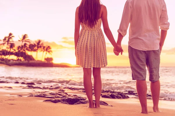 Pareja por detrás relajante viendo atardecer en la playa hawaiana juntos tomados de la mano Imagen de archivo