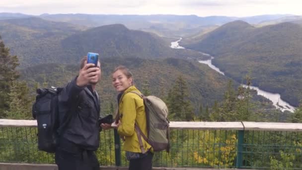 Πεζοπορία ζευγάρι με σακίδια στο Εθνικό Πάρκο του Κεμπέκ το φθινόπωρο, λαμβάνοντας selfie φωτογραφίες στον Καναδά δάσος ταξιδιωτικό τρόπο ζωής. Τουρίστες βλέπουν το Εθνικό Πάρκο Ζακ Καρτιέ — Αρχείο Βίντεο