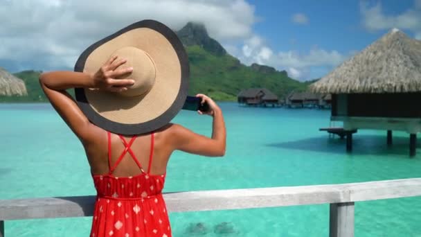 Viagens de luxo férias. Tourist woman using phone to take photo at view of ocean and mountain landscape on Bora Bora, Polinésia Francesa, Taiti. Vida luxuosa estilo de vida resort — Vídeo de Stock