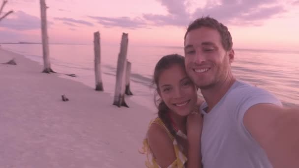夕日のビーチでロマンチックな美しい若いカップルによるセルフィービデオ夏の新婚旅行の旅行でリラックスしたカップルは、ラバーズキーで夕日を見て、フロリダ州フォートマイヤーズビーチの近く. — ストック動画
