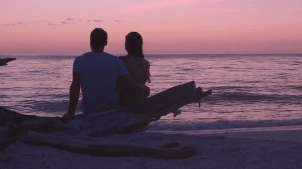 Romantická pláž západ slunce pár líbánky - Milenci se těší sledování západu slunce na letní cestování cíl sedí na kmeni stromu u oceánu. From Lovers key, Florida near Fort Myers Beach, USA — Stock video