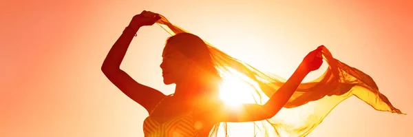 Hermosa mujer feliz libre en verano puesta del sol resplandor agitando bufanda en el viento bailando en la bandera panorámica del sol. Silueta femenina dama libertad para el bienestar y la vida saludable — Foto de Stock