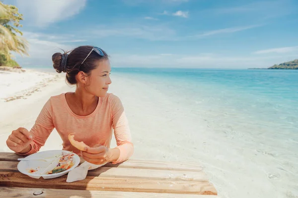 Tour di motu picnic sulla spiaggia della Polinesia Francese a Huahine, Tahiti, Polinesia Francese. Donna turistica felice mangiare a tavola in piedi acqua dell'oceano nella sabbia per il pranzo estivo. Stile di vita di viaggio — Foto Stock