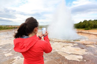 Tourist taking photos of geyser Strokkur clipart