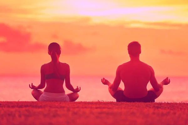 Pareja meditando al atardecer en la playa — Foto de Stock