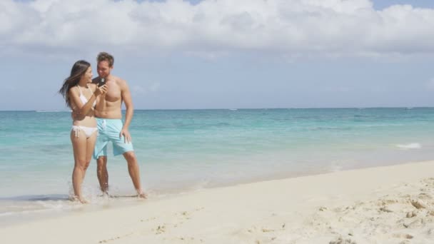 Casal usando telefone inteligente na praia — Vídeo de Stock