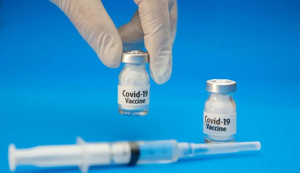 医療専門家は青い背景に注射器とCovid 19ワクチンの瓶を保持しています — ストック写真