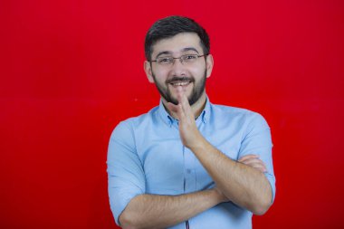 Kırmızı izole edilmiş arka planda, sade mavi gömlekli bir adam gülümser ve parmağını kameraya doğrultur..