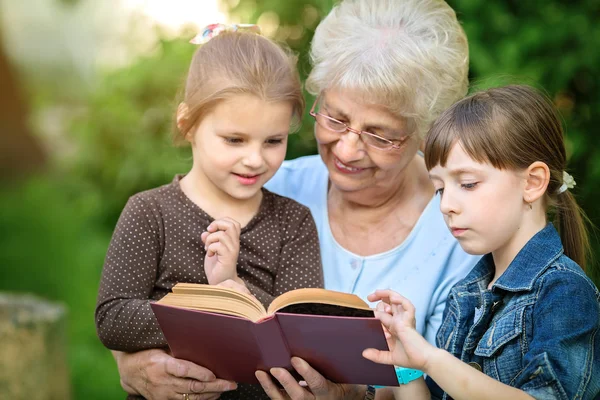 Concept d'éducation, grand-mère lisant un livre pour petits-enfants — Photo