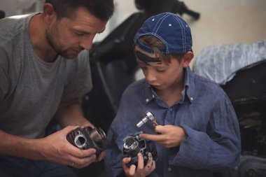Baba tamirci ve oğlu tamirhanedeki arabayı inceliyor.