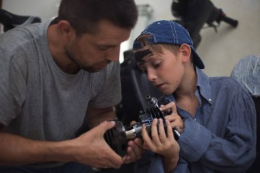 Baba tamirci ve oğlu tamirhanedeki arabayı inceliyor.