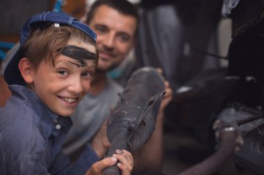 Baba tamirci ve oğlu tamirhanedeki arabayı inceliyor.