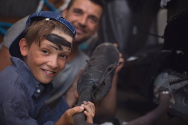 Baba tamirci ve oğlu tamirhanedeki arabayı inceliyor.