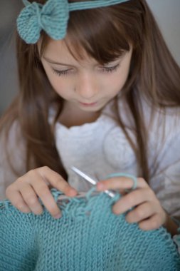 Evinde örgü iğnesiyle örgü ören küçük şirin bir kızın yakın portresi.