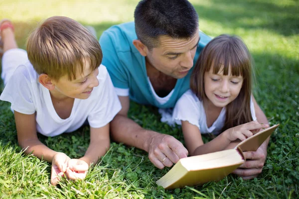 Far Läser Bok För Sina Barn När Han Ligger Utomhus — Stockfoto