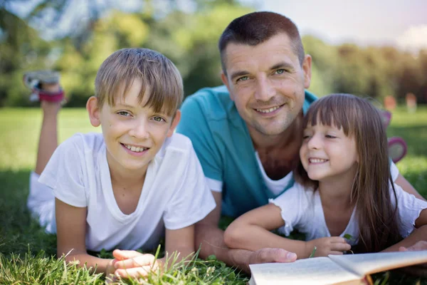 Far Läser Bok För Sina Barn När Han Ligger Utomhus — Stockfoto