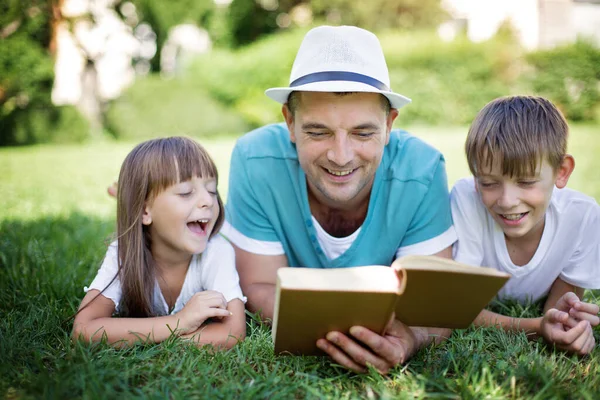 父亲一边给孩子们读书 一边把书放在公园的草地上 — 图库照片
